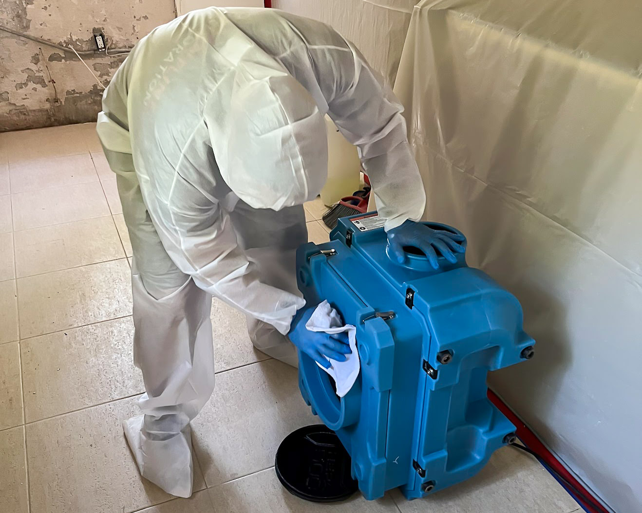 White-suited specialist positioning blue air mover during odor treatment
