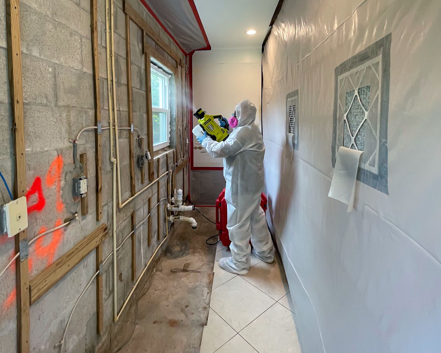 PPE-suited specialist applying odor neutralization treatment with electric sprayer inside containment zone