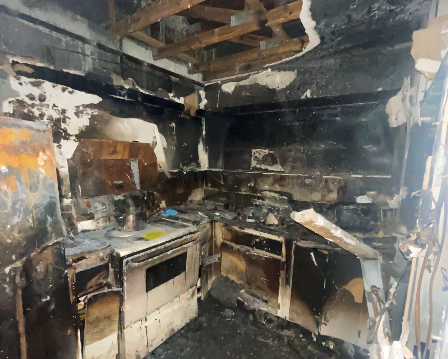 Completely fire-damaged kitchen — black soot covers all surfaces, ceiling burned through