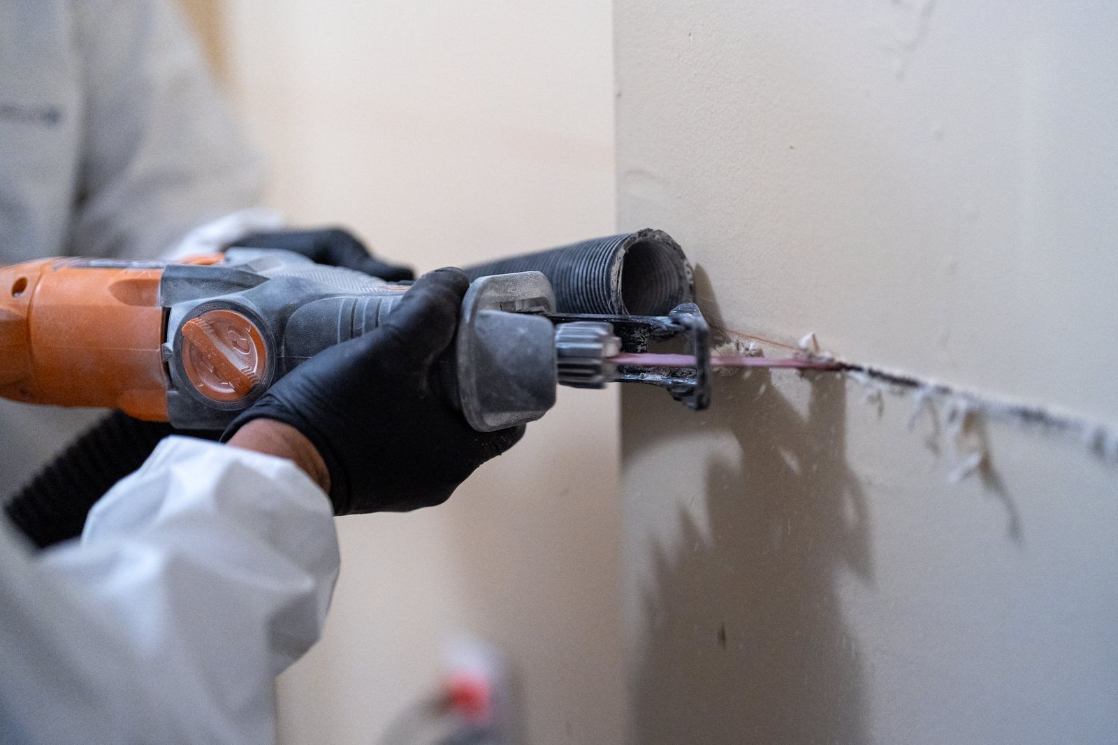Gloved hands performing controlled removal of damaged wall material