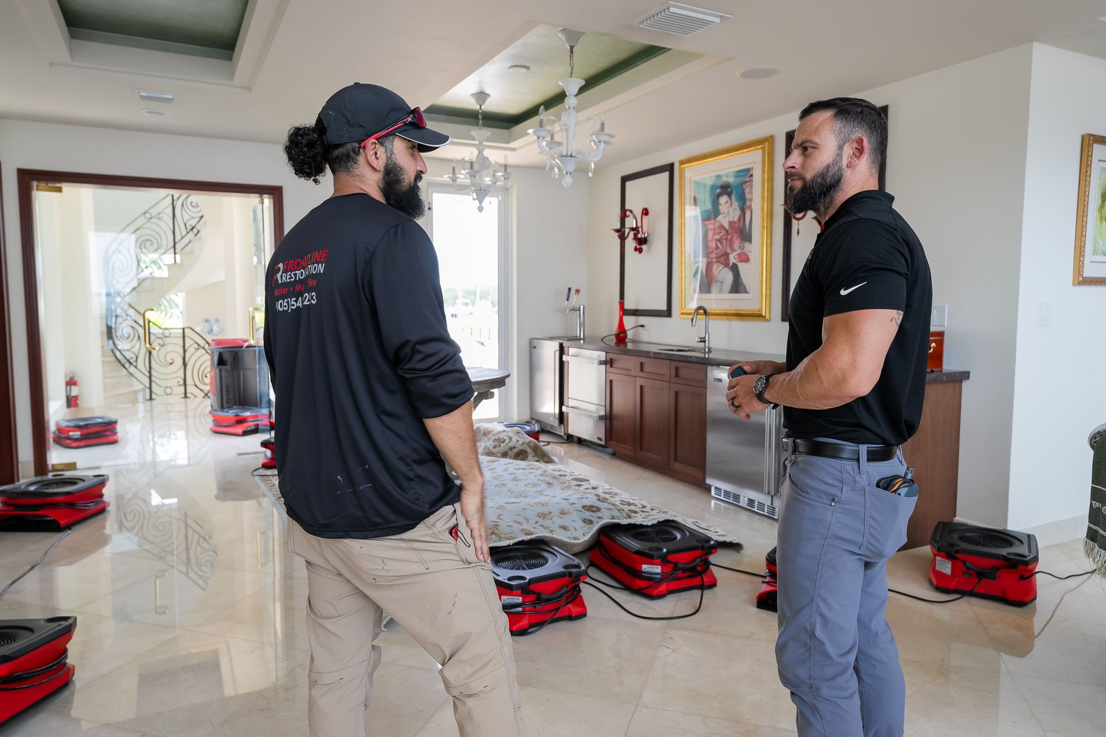 Two technicians assessing a water loss in a home with drying equipment in place