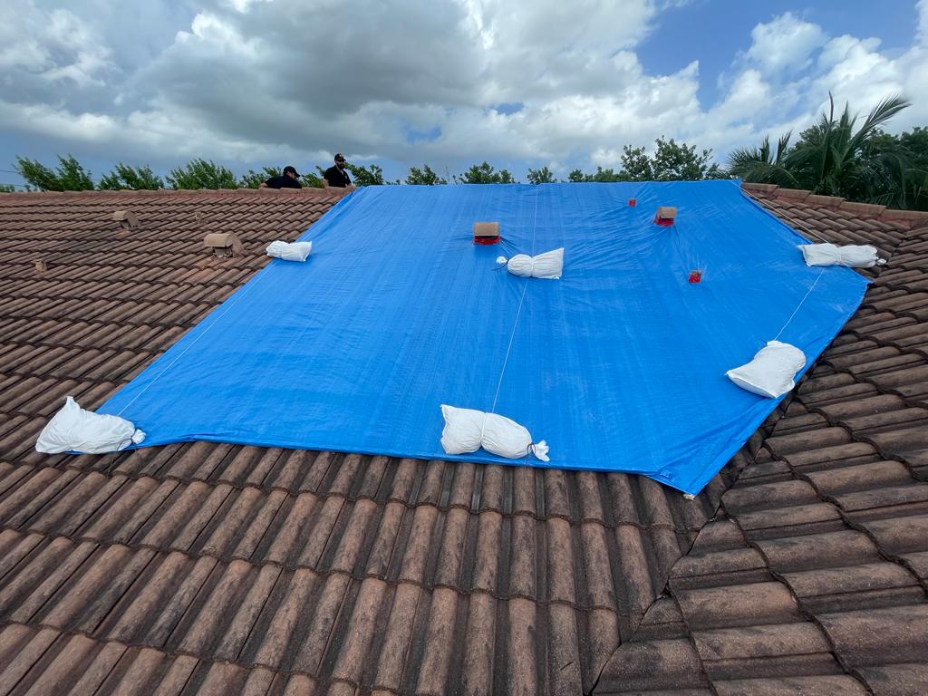 Frontline Restoration crew installing blue tarp on damaged tile roof with storm clouds overhead